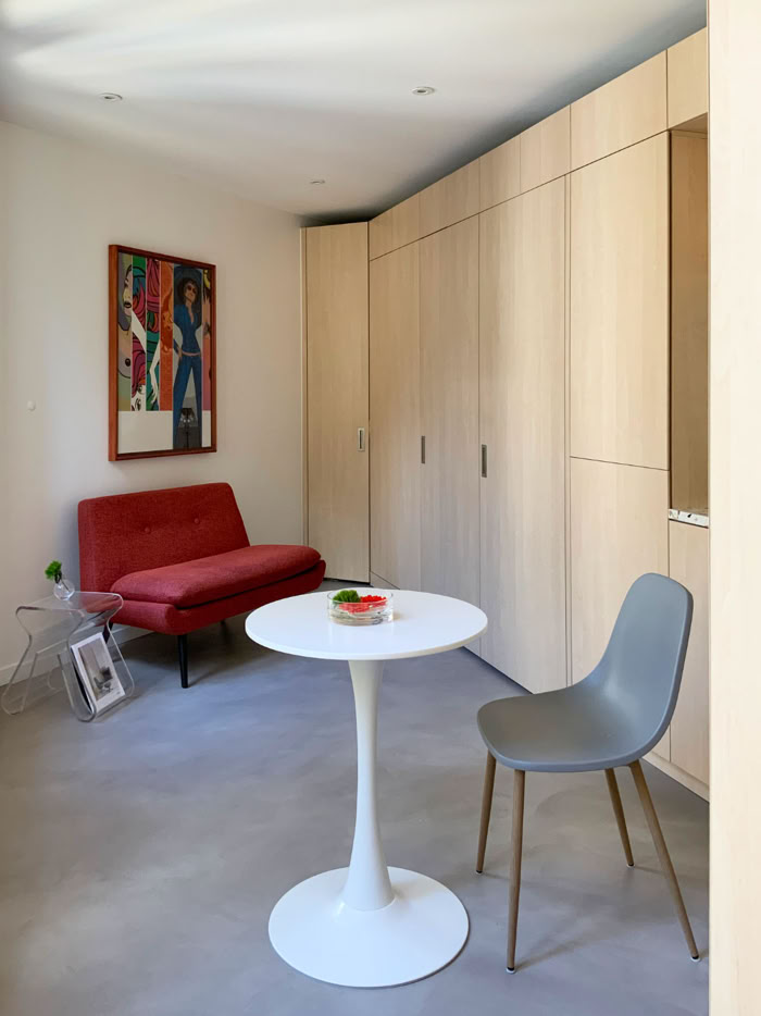 Vue d'ensemble d'un studio optimisé avec sol en béton ciré et mobilier sur mesure en stratifié bouleau.