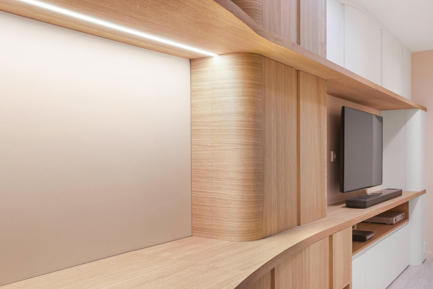 Détail d'une bibliothèque aux lignes courbes avec ruban LED intégré sous étagère en bois, rénovation à Metz et en Moselle.