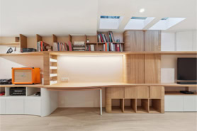 Espace bureau escamotable intégré dans une grande bibliothèque en bois clair avec éclairage LED, par un architecte d’intérieur à Metz.