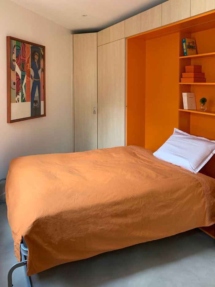 Lit escamotable ouvert formant paravent pour créer une zone nuit intime dans une pièce unique.