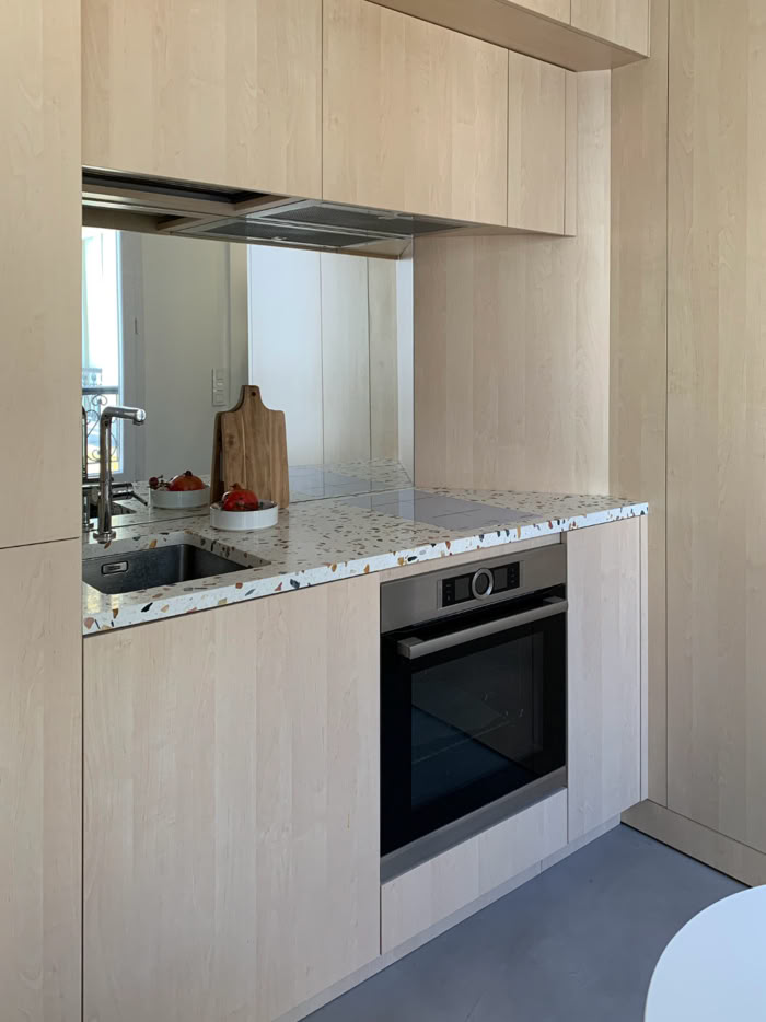 Cuisine minimaliste avec plan de travail en terrazzo et électroménager encastré pour petit appartement.