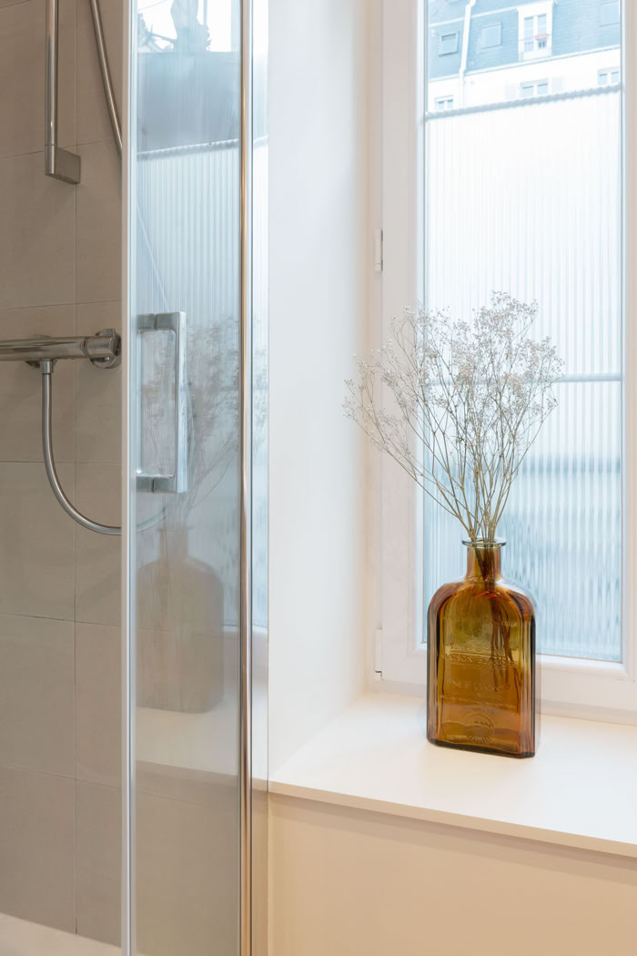 Zoom sur le rebord de fenêtre en salle d'eau, décoration sobre et apport de lumière naturelle.