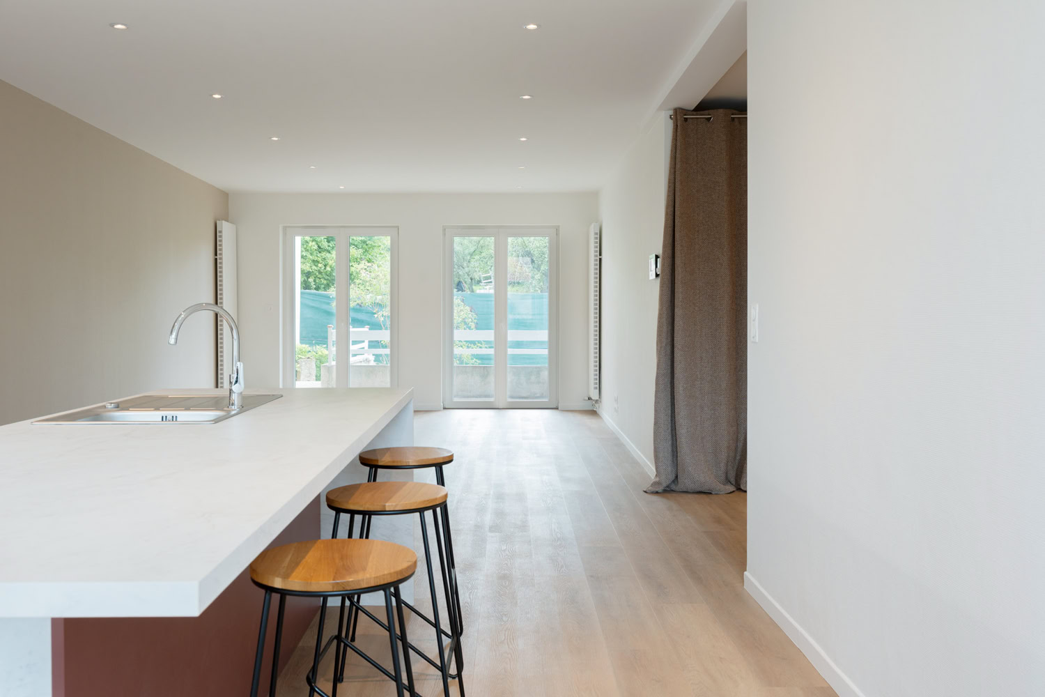 Cuisine ouverte avec îlot central blanc et tabourets en bois, rénovation maison Moselle.