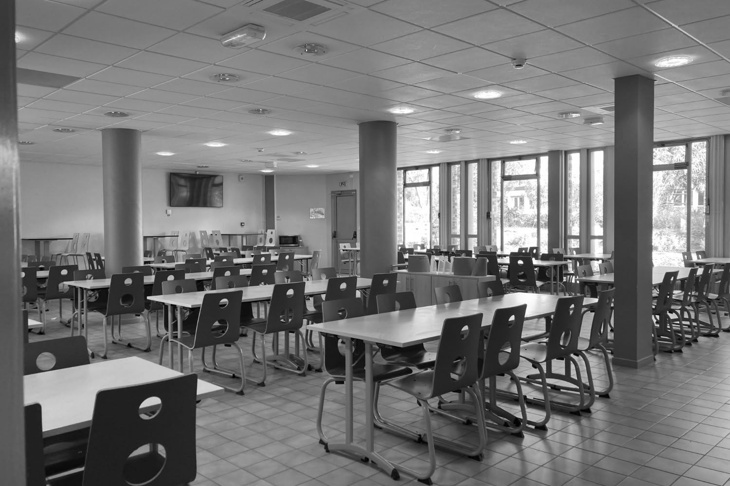 Intérieur de la salle à manger existante, montrant les tables, les chaises et la vue vers l'extérieur.