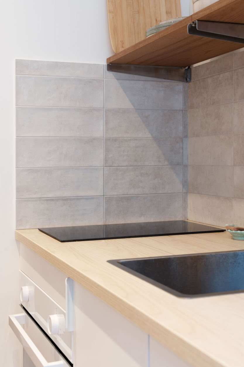 Détail de la crédence en carrelage gris et plaques de cuisson, matériaux durables.