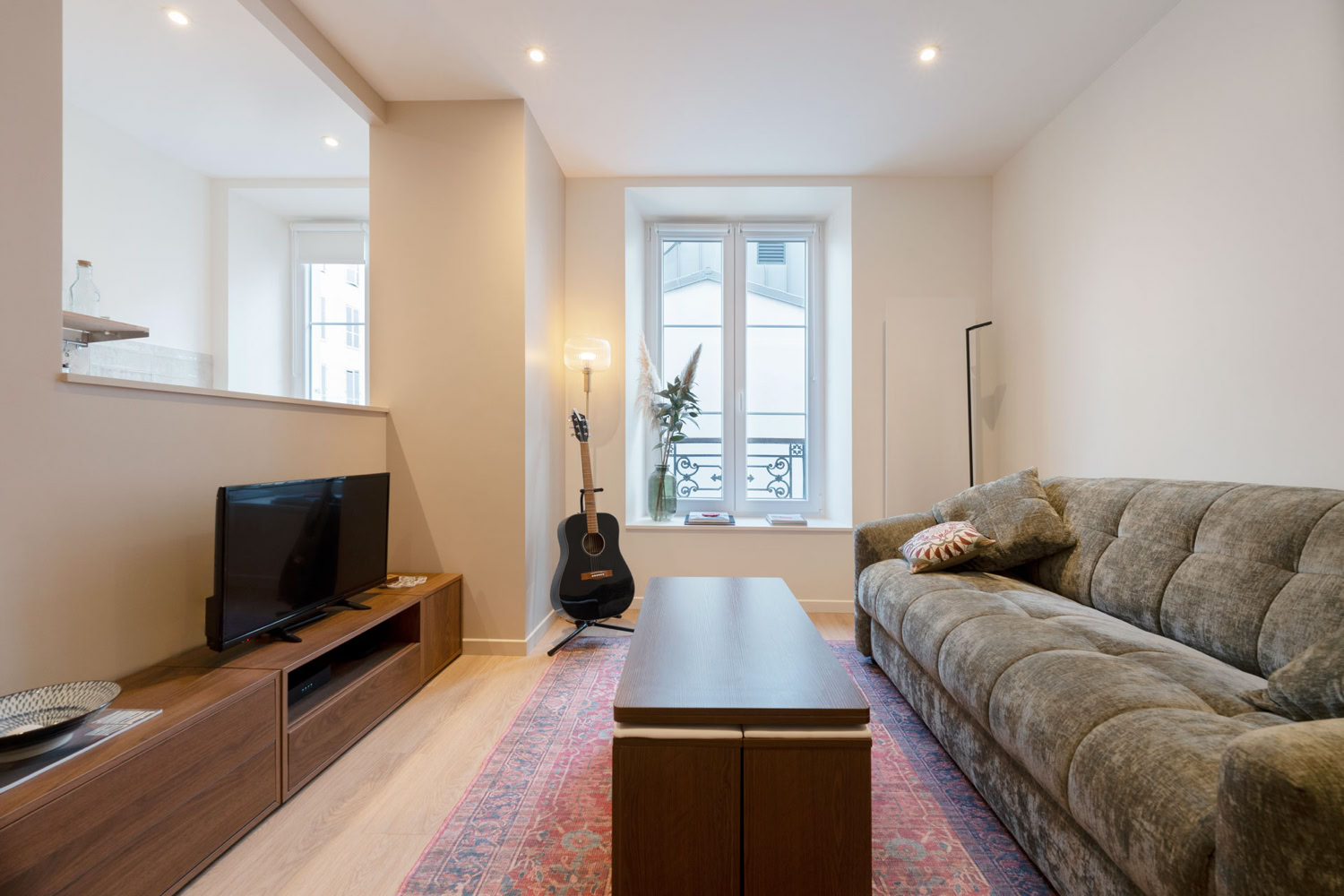Espace de vie complet avec meuble TV en bois et vue sur l'enfilade des fenêtres.
